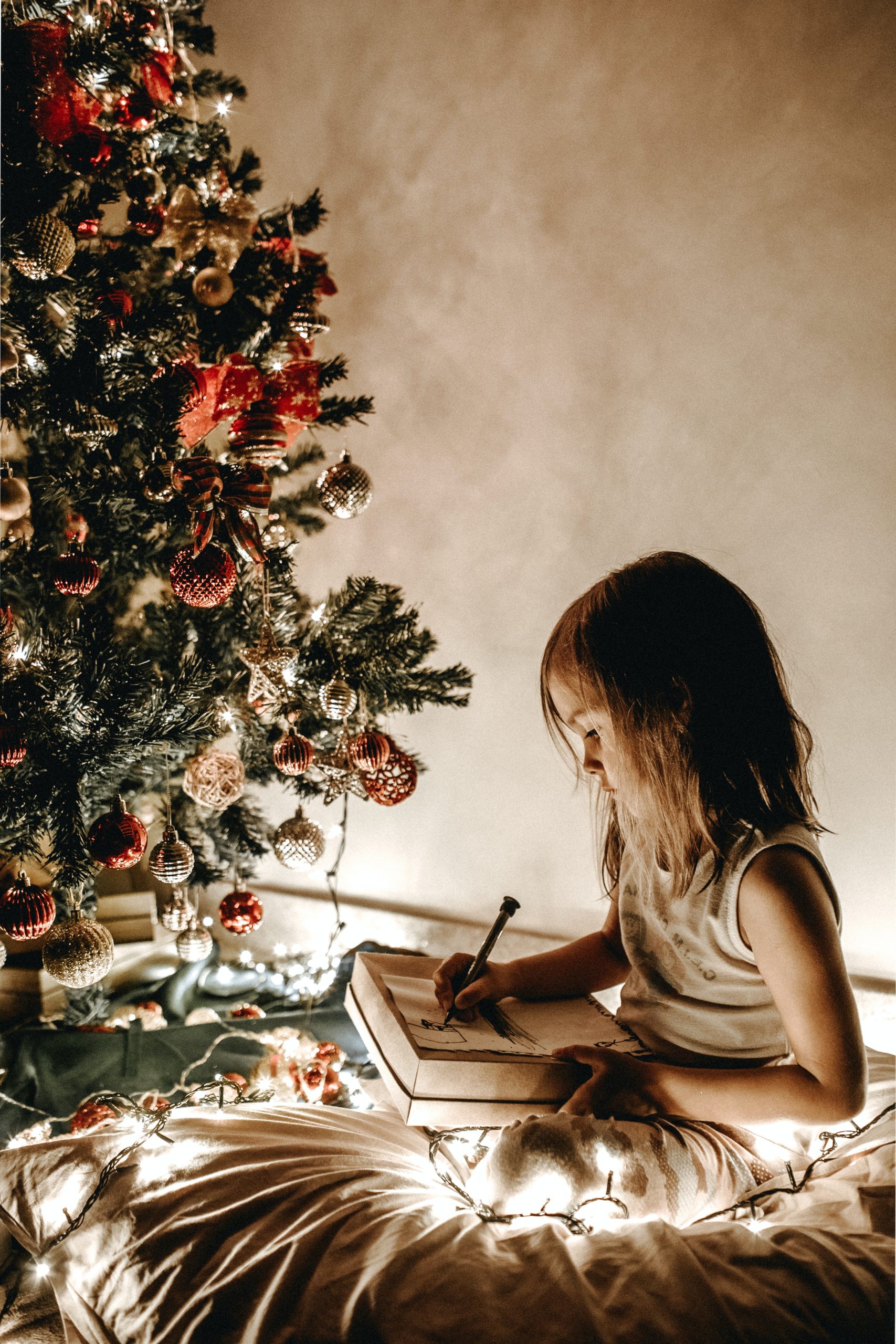 young girl writing next to Christmas tree