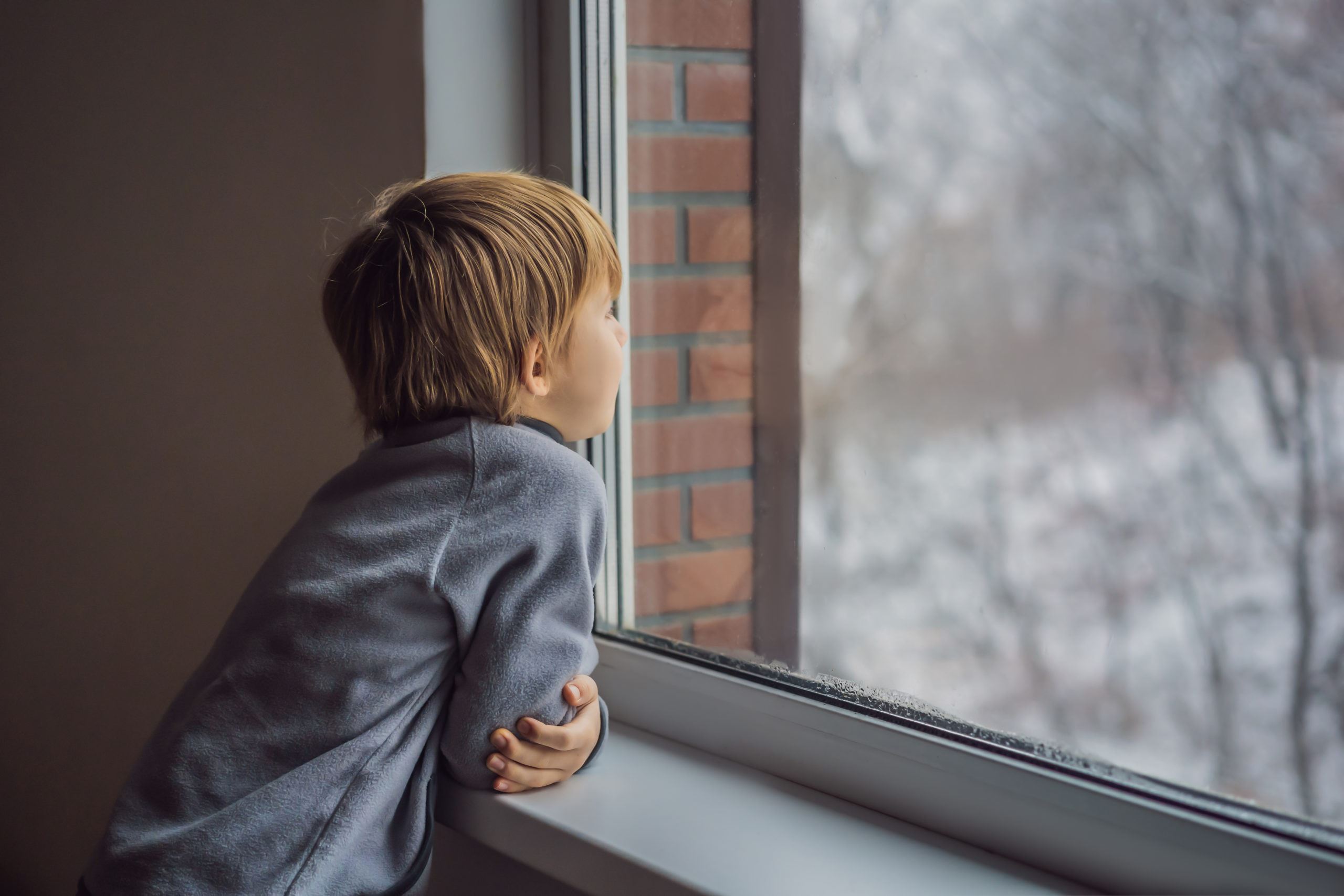 Child looking out a window alone